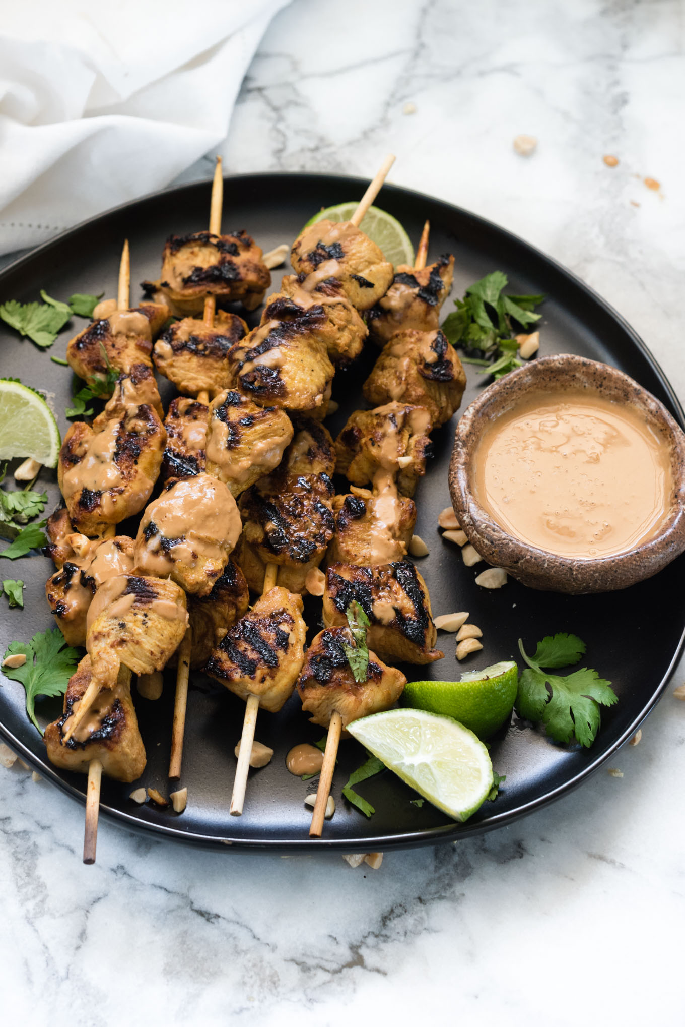 Chicken Satay on a black plate with peanut sauce and lime wedges