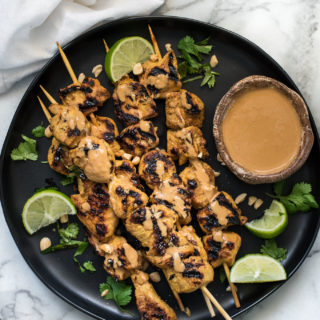 Chicken Satay on a black plate with peanut sauce